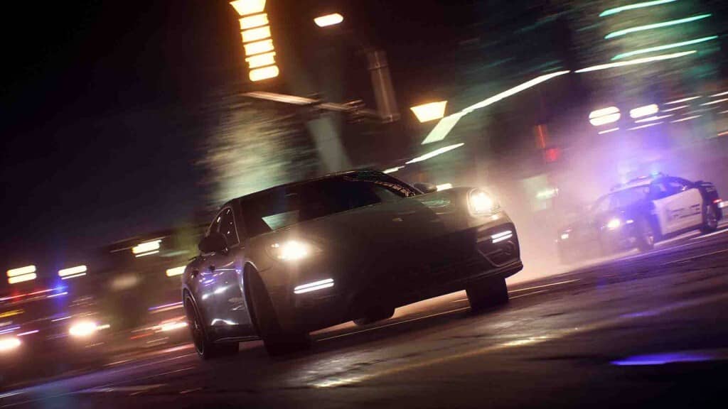 "Cảnh rượt đuổi tốc độ cao với xe cảnh sát trong Need for Speed Payback" Ảnh gameplay Need for Speed Payback, một chiếc xe đua màu đen đang chạy tốc độ cao vào ban đêm, tạo ra hiệu ứng vệt sáng mờ. Bên cạnh là chiếc xe cảnh sát với đèn nhấp nháy đang đuổi theo. Bối cảnh là đường phố đô thị về đêm.