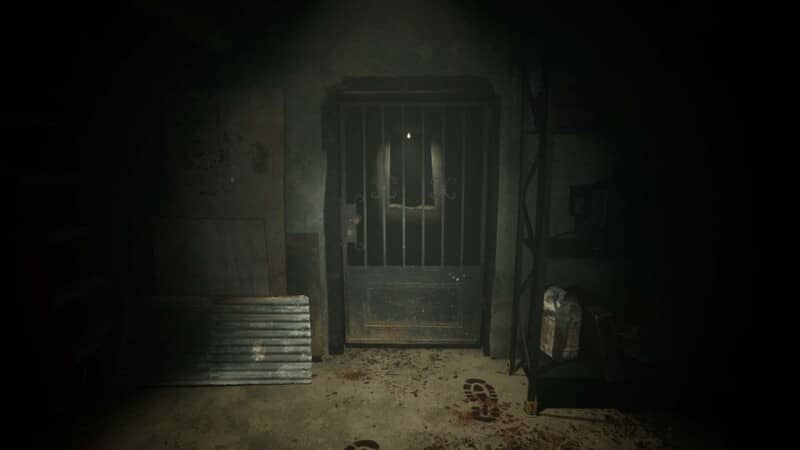 Cảnh trong ngục tối của game Slackjaw Ảnh gameplay game Slackjaw, một cánh cửa nhà tù bị khóa trong một căn phòng tối, trên sàn nhà có vết máu. Bối cảnh tạo cảm giác tù túng và nguy hiểm.